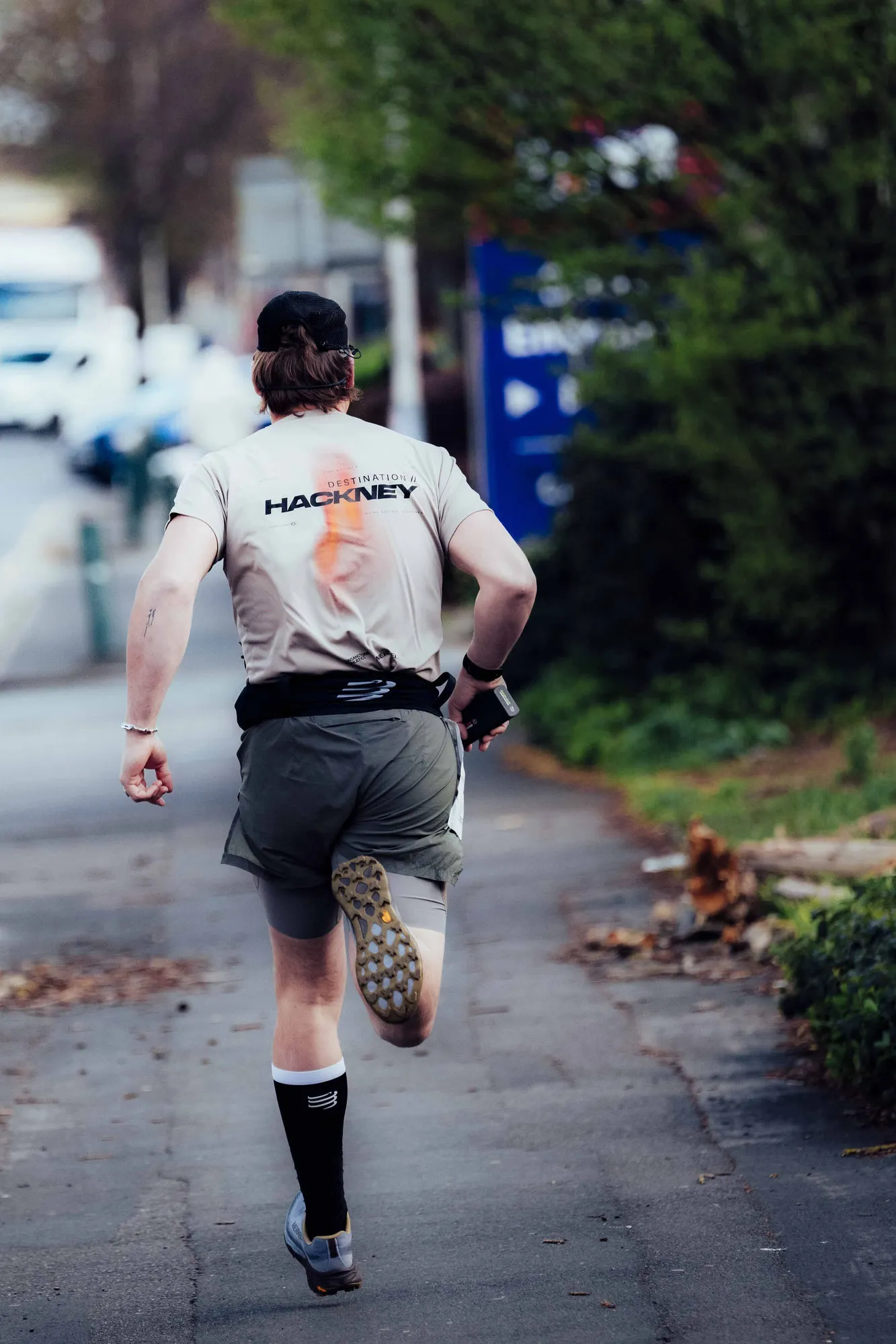 A relay runner mid-race carrying a RunnerBeam baton tracker in hand